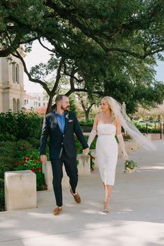 a bride and groom walking down the sidewalk holding hands