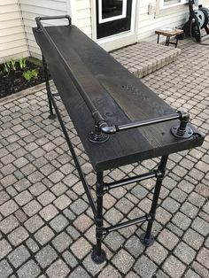 an outdoor table made out of metal pipes and wood with wheels on the legs, sitting in front of a house