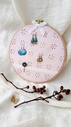 a pink embroidery hoop with earrings hanging from it's sides and on top of a branch