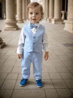 a little boy in a blue suit and bow tie is standing on the sidewalk near pillars