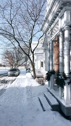 a house covered in snow next to a tree and cars parked on the side of the road