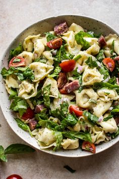 a white bowl filled with pasta salad on top of a table next to tomatoes and lettuce