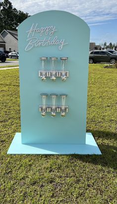 a blue birthday sign with candles on it in the middle of a grassy area next to a house