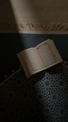 an open book sitting on top of a rug next to a wall with a light coming through it