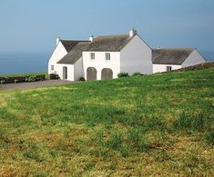 a large white house sitting on top of a lush green hillside next to the ocean