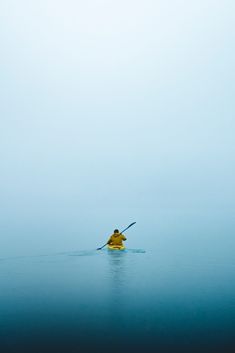 a person in a yellow kayak paddling through the water on a foggy day