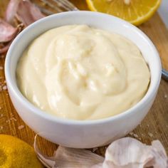 an easy garlic aioli recipe in a white bowl with lemons and garlic on the side