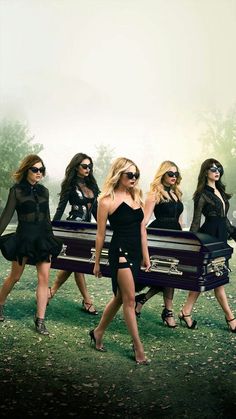 four beautiful women in black dresses and sunglasses walking with an old trunk on the grass