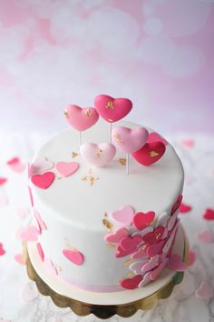 a white cake with pink hearts on top and gold decoration around the edges, sitting on a table