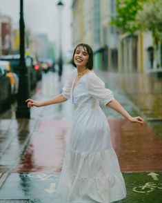 a woman in a white dress is standing on the sidewalk with her arms spread out