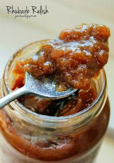 a spoon with some food in it on top of a glass jar filled with jelly