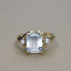 Vintage 14k gold ring set with a rectangular cut synthetic (lab made) blue spinel. The stone is flanked by a white seed pearl on each shoulder. The front of the band had a knife edge design. Era: c.1960s Markings: 14k, WB (maker's mark) Materials: 14k gold, seed pearls (2.5 mm each), synthetic blue spinel (8.25mm x 5.53mm)  Ring Size: 5 3/4 (comes with one free resizing by our jeweler. Just add your size to the order notes) Weight: 2.8 grams Condition: Excellent vintage condition with minor wear Elegant Rectangular Topaz Ring In 14k Gold, Elegant 14k Gold Rectangular Topaz Ring, Rectangular Topaz Wedding Ring In 14k Gold, Rectangular Birthstone Ring For Formal Occasions, Classic Rectangular Gemstone Birthstone Ring, Formal Rectangular Topaz Ring In 14k Gold, Classic Rectangular Birthstone Ring, Classic Rectangular Birthstone Ring For Wedding, Classic Rectangular Birthstone Wedding Ring