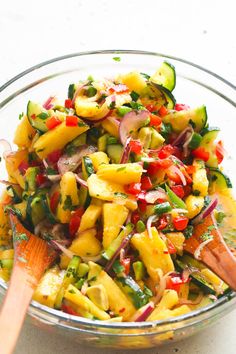 a glass bowl filled with mixed vegetables on top of a wooden spoon and serving utensils