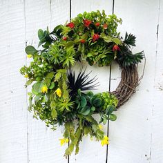 a wreath is hanging on the side of a white wall with flowers and plants around it