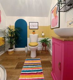 a bathroom with yellow and blue walls, wood flooring and pink cabinets