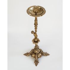 an antique brass candle holder with flowers and leaves on the base, standing upright against a white background