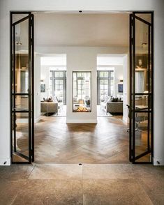 an open door leading into a living room with white walls and wood floors, in front of two couches