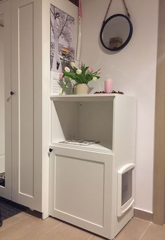 a white cabinet with flowers in it and a mirror hanging on the wall behind it