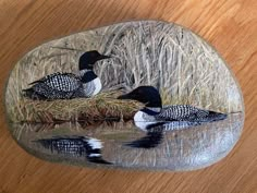 two birds sitting on top of a rock in the water next to some dry grass