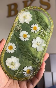 a hand holding a green and white flowered cell phone case with gold glitter border