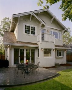 a large white house with a patio and table in the front yard, surrounded by grass