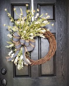 a wreath on the front door with flowers and ribbon hanging from it's side