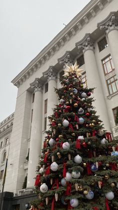 a large christmas tree in front of a white building with red and gold ornaments on it