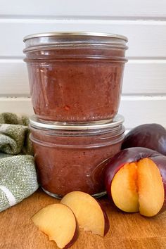 two jars filled with food sitting on top of a wooden table next to sliced plums