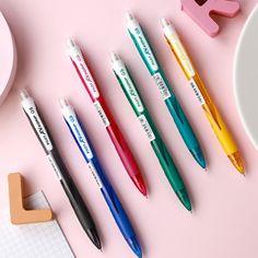 five pens lined up next to each other on top of a pink surface with letters and numbers