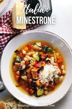 a bowl of minestone soup with cheese and bread on the side next to it