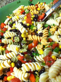 a green bowl filled with pasta salad on top of a table next to a fork