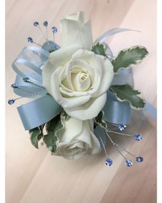 a white rose and blue ribbon corsage on a wooden table with beads, leaves and ribbons