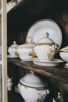 white and gold dishes are on shelves in a room with wood trimmings,