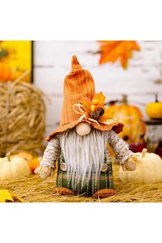 an orange and white gnome figurine sitting on hay with pumpkins in the background