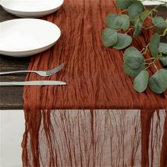 the table is set with silverware, plates and greenery on top of it