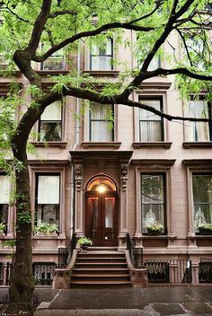 an apartment building with stairs leading up to the front door and trees in front of it