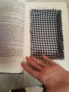 a person holding an open book in their left hand, next to a piece of fabric