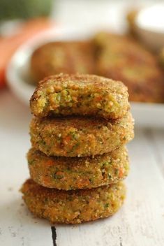 three carrot patties stacked on top of each other in front of a plate of carrots