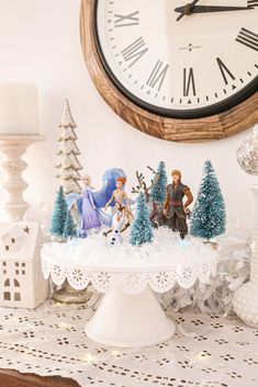 a table topped with figurines next to a clock and christmas trees on top of it