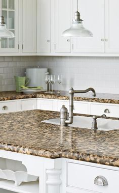 a kitchen with white cabinets and granite counter tops, two pendant lights over the sink