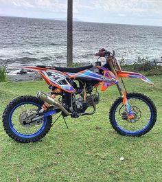 a dirt bike parked on top of a lush green field next to the ocean in front of a body of water