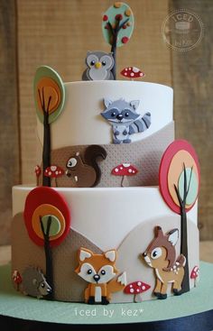 a three tiered cake with woodland animals on it's side and trees in the background