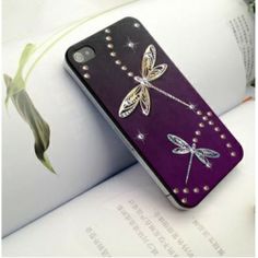 a purple phone case with dragonflies on it sitting on top of an open book