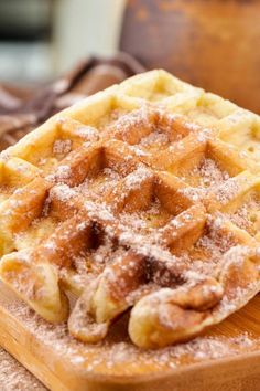 a waffle sitting on top of a wooden cutting board covered in powdered sugar