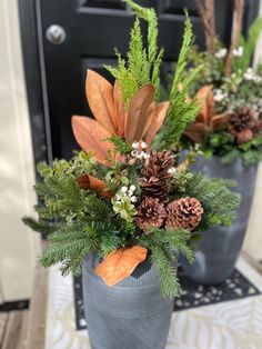 two vases filled with plants and pine cones on top of a table next to a door