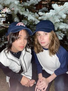 two young women sitting next to each other on the ground in front of a tree