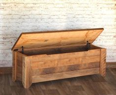 an empty wooden box sitting on top of a hard wood floor next to a brick wall