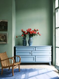 two vases with flowers sit on top of a blue dresser in a green room