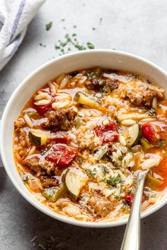 a bowl of soup with meat, vegetables and pasta in it next to a spoon