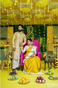 a man and woman sitting on a chair in front of a yellow wall with decorations